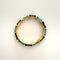Gold bracelet with black and green accents on a light beige background