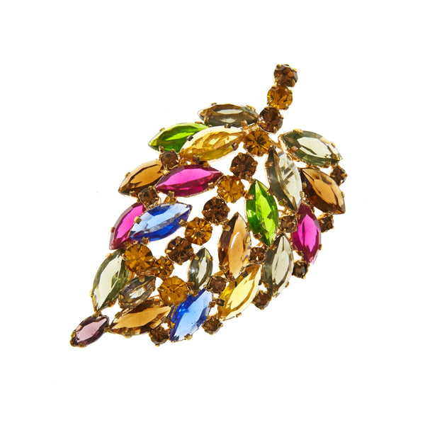 A gold-toned leaf-shaped brooch embellished with multicolored marquise and round rhinestones in shades of yellow, green, blue, pink, and brown, set against a plain white background.