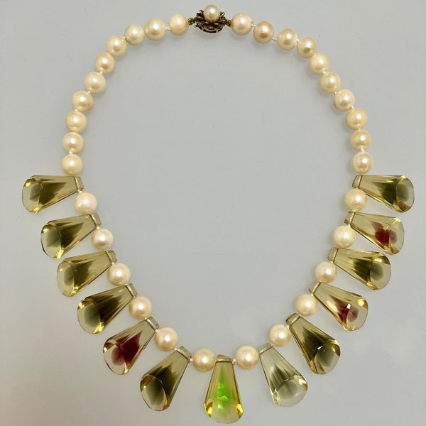 A vintage-style statement necklace featuring cream-colored faux pearls and faceted amber-yellow teardrop-shaped crystals, displayed against a neutral light gray background.