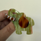 A hand holding a small elephant-shaped brooch. features a marbled green and white pattern with a glossy brown ear and trunk 