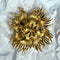A gold-toned sunburst brooch with a pin back, displayed on crumpled white paper.