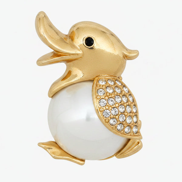 A gold plated duck brooch with a glossy white pearl body and a wing encrusted with clear rhinestones, shown on a white background