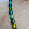 Necklace with green and blue beads on a textured beige background