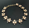 A gold-tone chain necklace featuring multiple floral clusters of pale peach-pink beads with clear faceted rhinestones, displayed on a dark gray background.