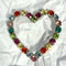 A heart-shaped brooch made of colourful round rhinestones in red, orange, pink, green, blue, and yellow, set in silver-toned metal, displayed on a crumpled white paper background.