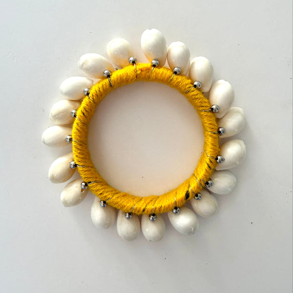 A handmade bangle featuring a bright yellow yarn-wrapped center band, surrounded by shells photographed from directly above on a plain light background.