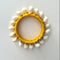 A handmade bangle featuring a bright yellow yarn-wrapped center band, surrounded by shells photographed from directly above on a plain light background.