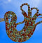 A decorative bird brooch like a stylized bird covered with many faceted rhinestones in gold, green, red, and blue tones against a blue sky background.