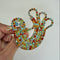 A hand holding a decorative, bird-shaped brooch covered in multicolored rhinestones against a plain white background.