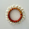 A bangle made of white cowrie shells arranged around a red and yellow wrapped bangle with small silver beads, photographed on a plain light background.