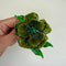 A hand holding a vintage-style green flower brooch with a central green gemstone, set against a plain off-white background.
