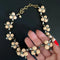 A gold-tone statement necklace with cream-colored flower-shaped beads and clear rhinestones, held in a hand against a dark background.