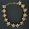 A vintage-style gold-tone chain necklace featuring alternating floral motifs with pale pink round beads and small dangling gold charms, displayed on a dark background.