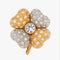 A gold and silver-tone four-petal flower brooch embellished with clear rhinestones, featuring a central round iridescent crystal on a clear gray background.