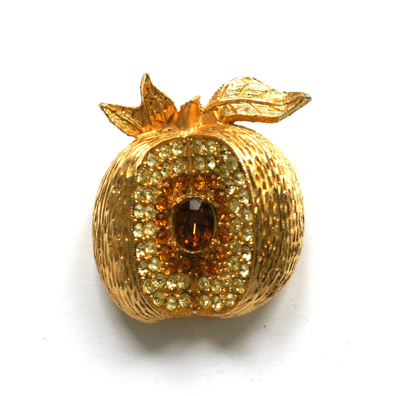 A gold-plated brooch in the shape of an apple, set with brown, topaz, and pale yellow crystals.